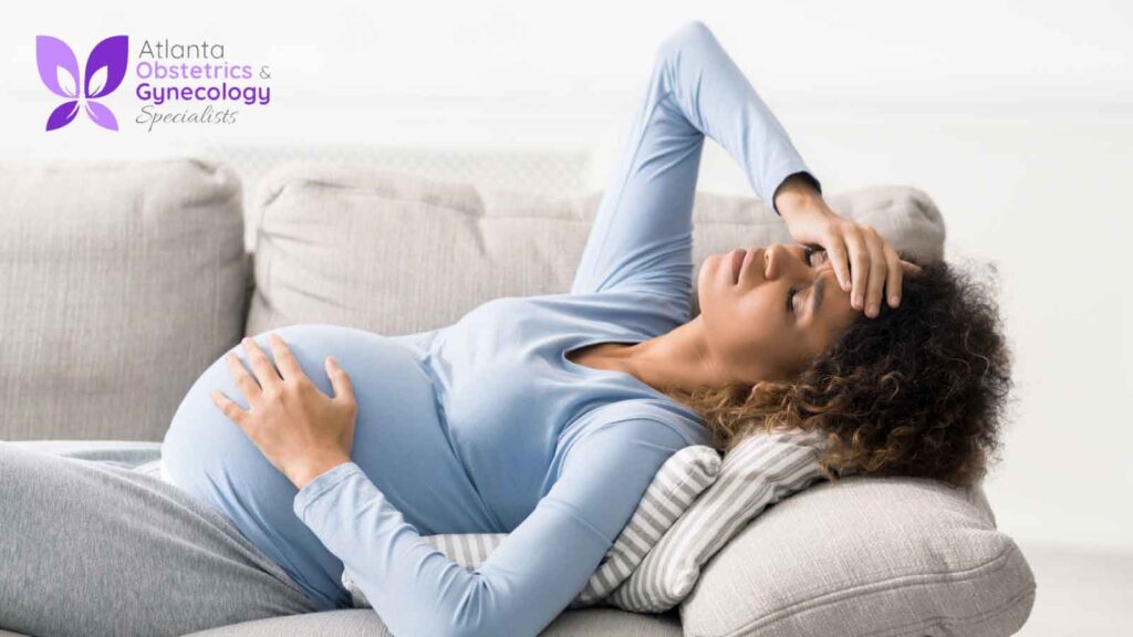 A pregnant woman lying comfortably on a sofa, holding her belly and forehead.