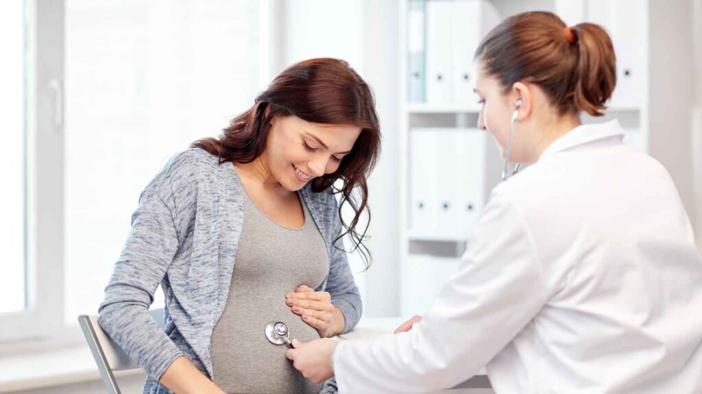 A pregnant woman sitting in a medical office, consulting with her OB-GYN during an appointment.