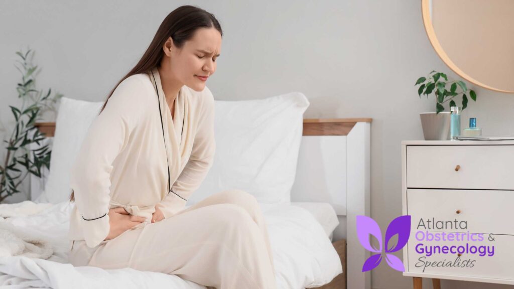 Young woman sitting on her bed holding her lower abdomen with a pained expression