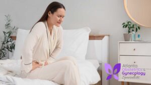 Young woman sitting on her bed holding her lower abdomen with a pained expression
