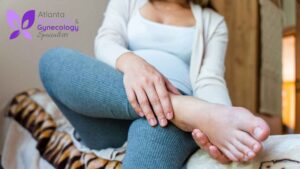 A pregnant woman sitting on her bed, gently holding her leg