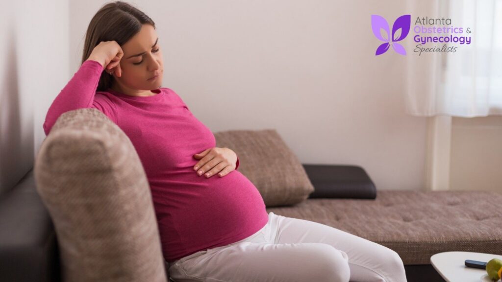 A pregnant woman sitting on a couch, touching her belly.