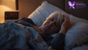 An older woman lying in bed at night, struggling with sleep disruption.